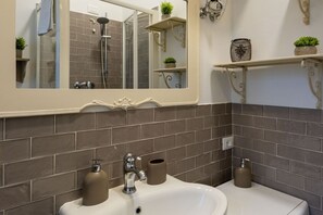 Un baño con un espejo grande, un lavabo con dos dispensadores de jabón, un perchero para toallas y una zona de ducha.