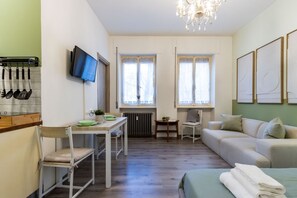 Una habitación compacta con kitchenette, una mesa de comedor, un sofá, un televisor y una araña.