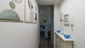 Un pasillo estrecho con una cama, un extintor y un baño con espejo, lavabo y toallero.