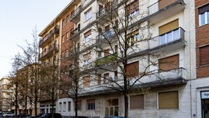 Un edificio residencial de varios pisos con balcones, una zona de estacionamiento y árboles en la parte delantera.
