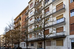 En flervåningsbyggnad med bostäder, balkonger, en parkeringsplats och träd framför.