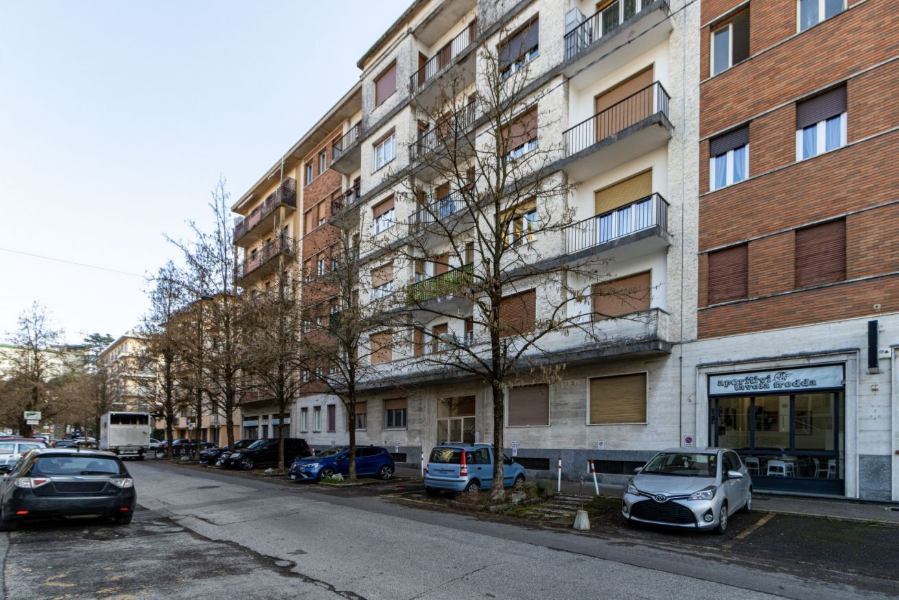 Ein mehrstöckiges Wohngebäude mit Balkonen, parkenden Autos und einem Geschäftslokal.