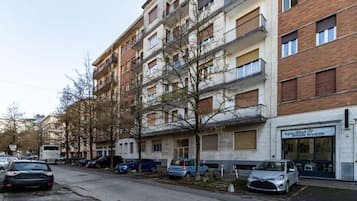 Ein mehrstöckiges Wohngebäude mit Balkonen, parkenden Autos und einem Geschäftslokal.
