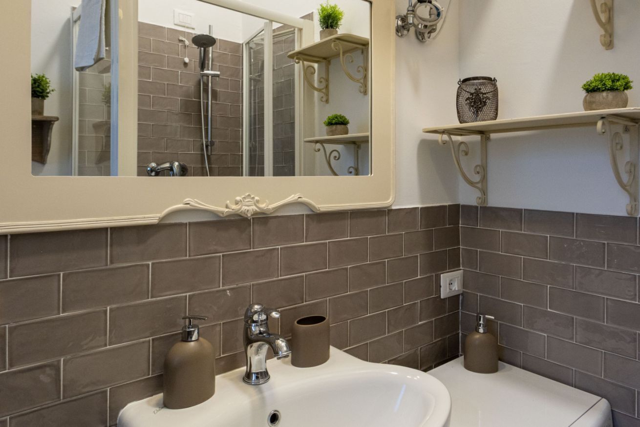 Un baño con un espejo grande, un lavabo con dos dispensadores de jabón, un perchero para toallas y una zona de ducha.