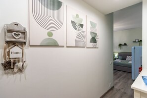 Ein modernes Interieur mit abstrakter Wandkunst, einem kleinen Holzregal mit herzförmigem Schmuckstück und einem Bett im Hintergrund.