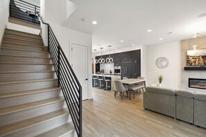 Un intérieur moderne comprenant un escalier en bois, un coin repas, une cuisine et un salon avec une cheminée.