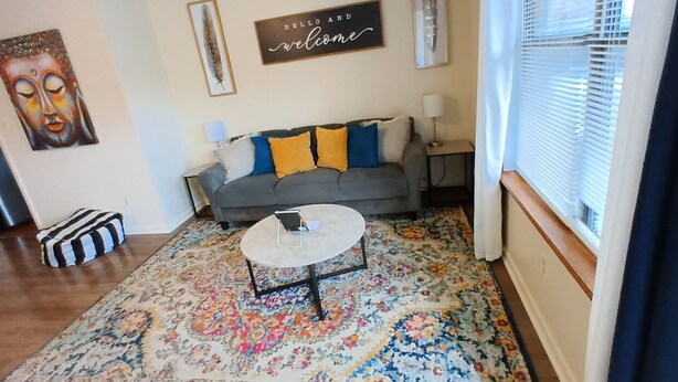 Ein Wohnzimmer mit grauem Sofa, farbenfrohem Teppich und einem runden Couchtisch.