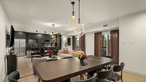 A modern kitchen with dark cabinetry, a dining area with a large table and chairs, and a living room with a sofa and a TV. - Resort-Style 4BR Ensuites •Slps11 •Pool&Spa •Gate (Houston)