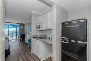 A compact kitchen with white cabinets, a black Galanz refrigerator, a microwave, and a granite countertop. - Oceanfront Escape | Pools | Sleeps 4 (Myrtle Beach)