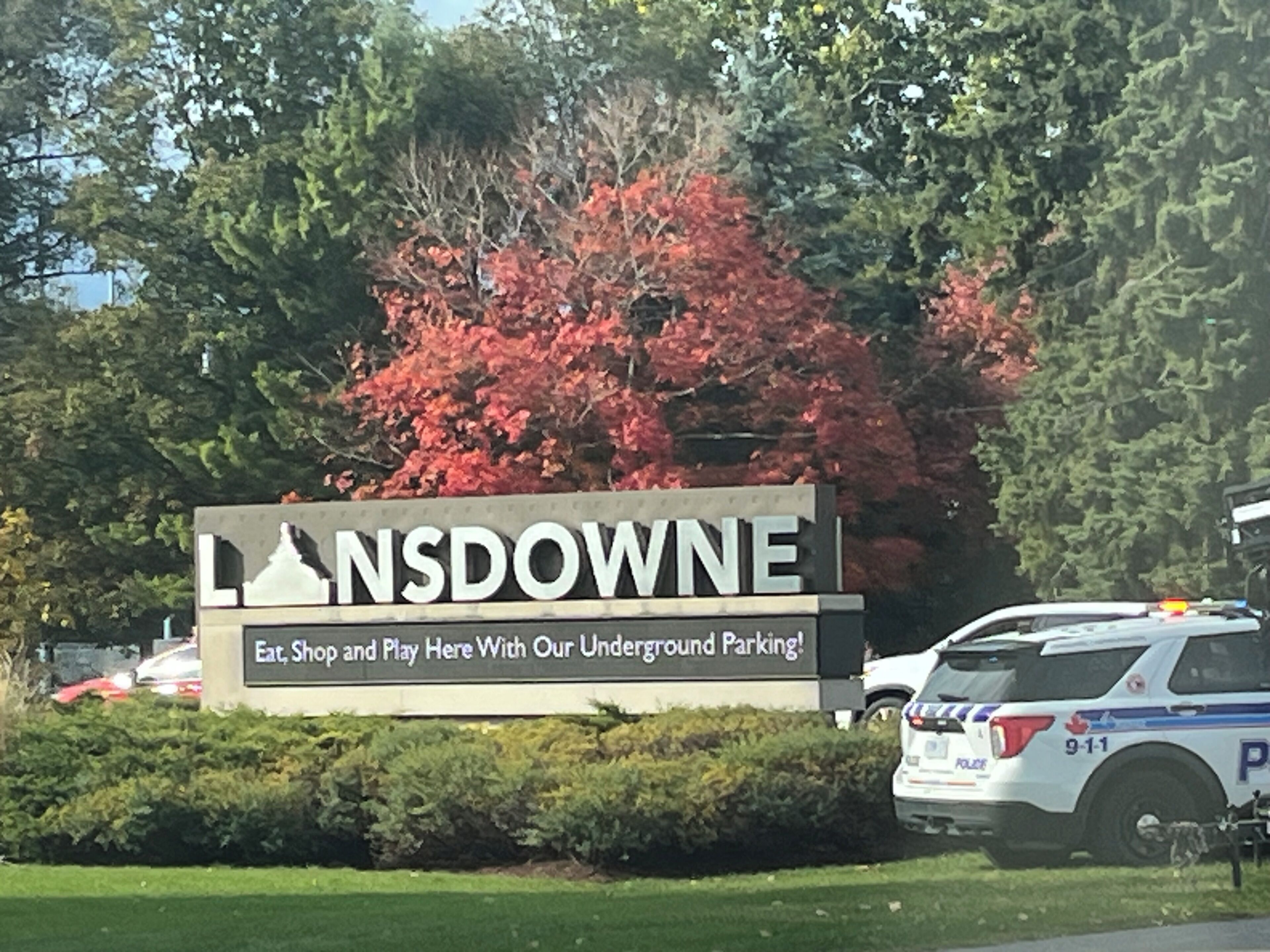 A sign for Lansdowne with underground parking, a police car, and trees in the background.