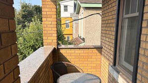 Un petit balcon avec une table ronde et deux chaises, des murs en briques et une fenêtre.