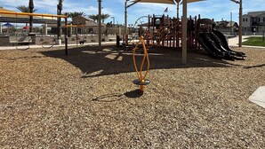 Ein Spielplatz mit schattigem Spielbereich, Schaukeln und einer Kletterkonstruktion.