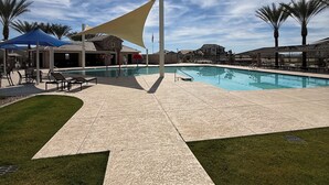 Ein Poolbereich mit blauem Himmel, Palmen und einer schattigen Sitzgelegenheit.