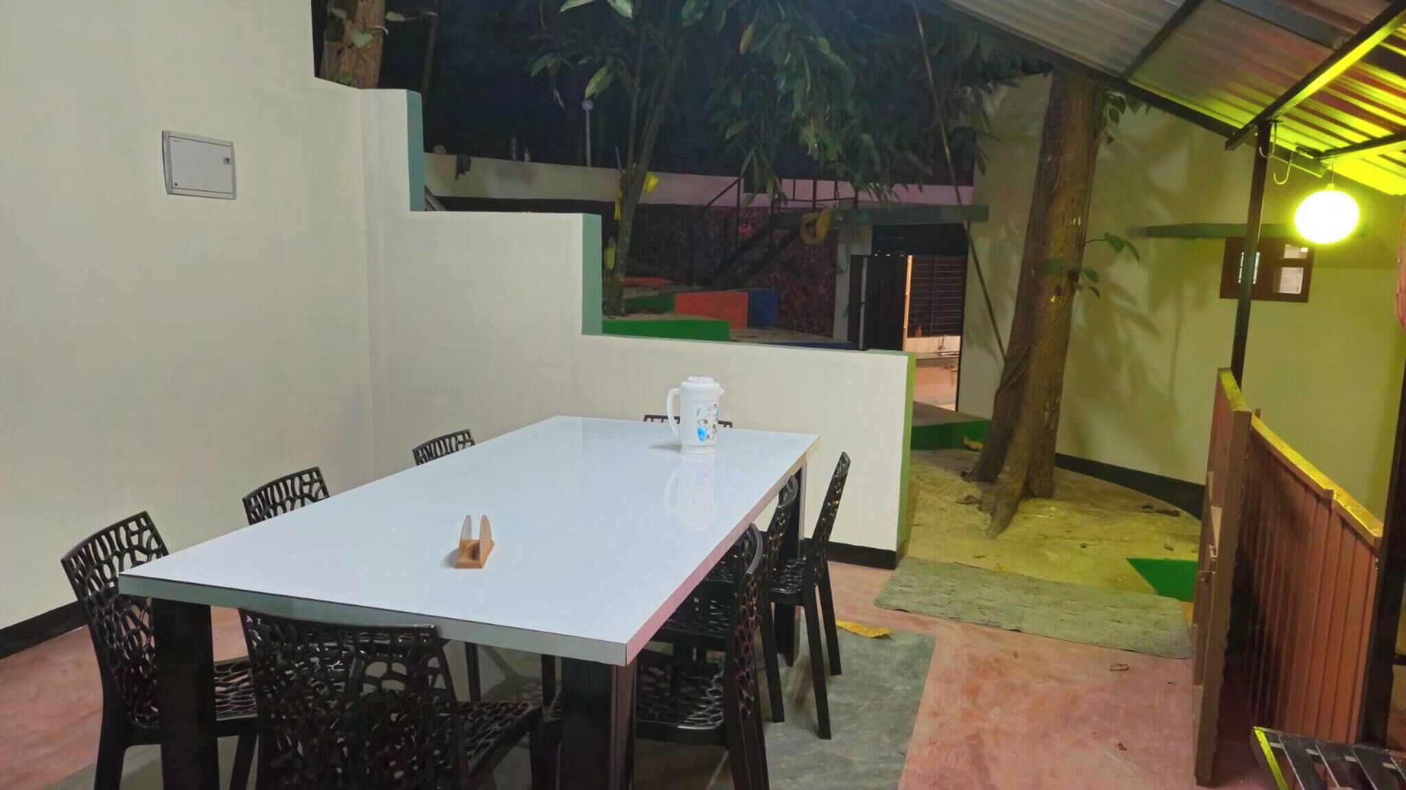 A dining area with a white table and black chairs, a coffee pot, and a small plant on the table.