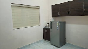 Eine kleine Küche mit Kühlschrank, einem Hängeschrank und einem Fenster mit Jalousien.