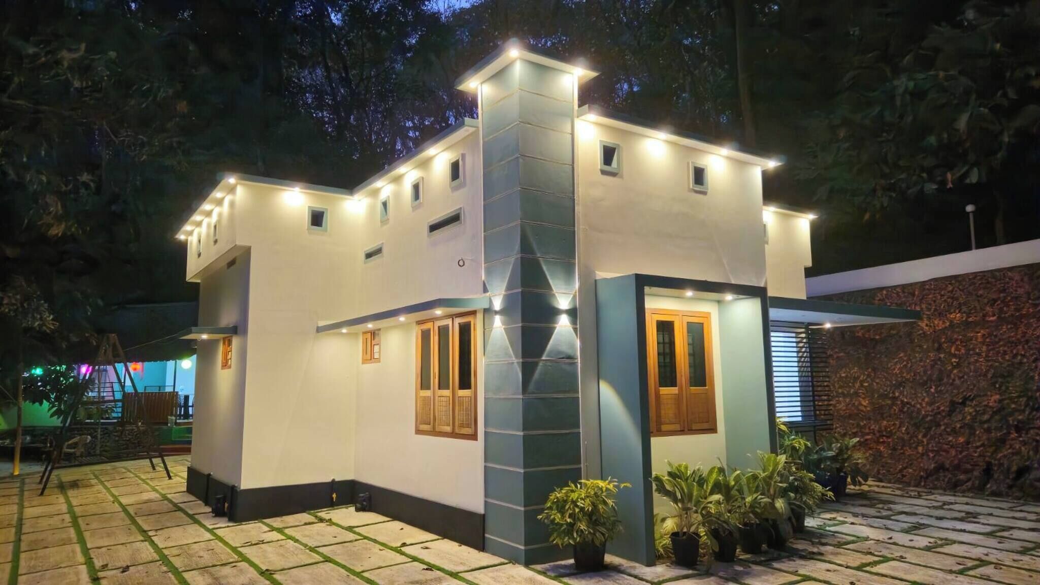 A modern house with a central tower, multiple windows, and a paved patio with potted plants.