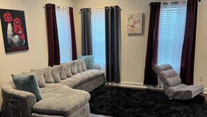 Ein Wohnzimmer mit einem Ecksofa, einem Liegesessel und einem schwarzen Teppich.