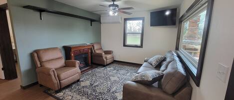 A living room with a fireplace, two leather armchairs, a sofa, a patterned rug, and a ceiling fan.