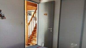 A bedroom with a bed, a wooden staircase, and a grey door. - Practical house, pets welcome - 6 guests (La Tranche-sur-Mer)