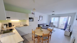 Een compact appartement met een kitchenette, een eethoek en een woonkamer met een bank en een fauteuil.