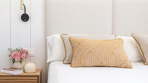 A neatly made bed with white and patterned pillows, a bedside table with a book and a vase of flowers, and a wall-mounted light fixture. - Apartment with private terrace - 4 guests (Málaga)