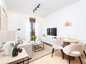 A modern living room with a sofa, coffee table, and chairs, a dining area with a table and chairs, a TV mounted on the wall, and a balcony with curtains. - Apartment with private terrace - 4 guests (Málaga)