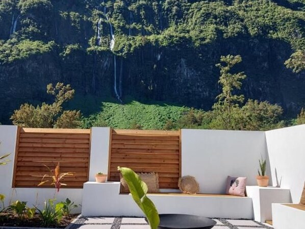 A modern outdoor seating area with a wooden fence, white walls, and a view of a lush green landscape with a waterfall.