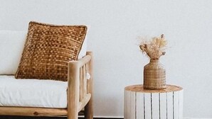 Een houten stoel met een geweven kussen en een klein houten tafeltje met een vaas droogbloemen.
