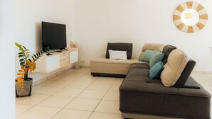 A modern living room with a flat-screen TV, a sofa set, a decorative wall clock, and a hanging light fixture.