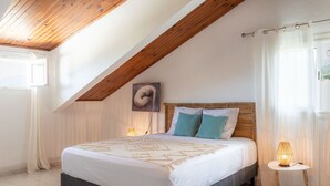 A bedroom with a sloped ceiling, a bed with a patterned bedspread, two pillows, a bedside lamp, and a woven rug.