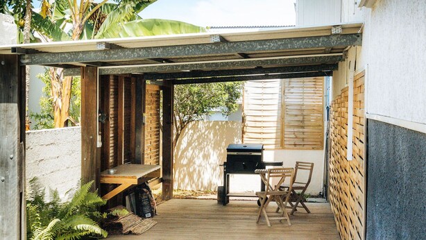 A covered outdoor patio with a grill, seating area, and a wooden deck.