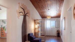 A hallway with wooden flooring, a blue armchair, a small stool, a bookshelf, and a wall-mounted tree decoration.