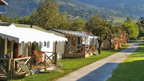 Fileira de casas móveis, com um caminho de cascalho, árvores e uma montanha ao fundo.