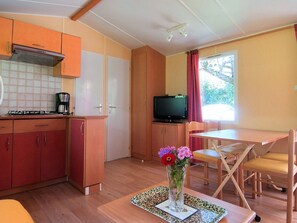 Eine kompakte Küche mit Gasherd, Kaffeemaschine und einem Fernseher auf einem Schrank. Ein Essbereich mit Tisch und Stühlen, und ein Blumenstrauß steht auf dem Tisch.