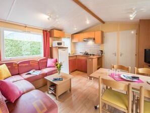 Ein gemütlicher Wohnraum mit Sofa, Esstisch, Küchenzeile und einem Fenster mit Blick ins Grüne.