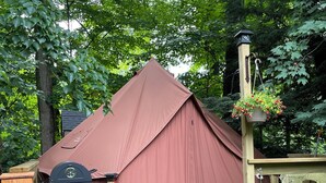 Una carpa con una parrilla, dos sillas de madera y un macramé colgante con flores.