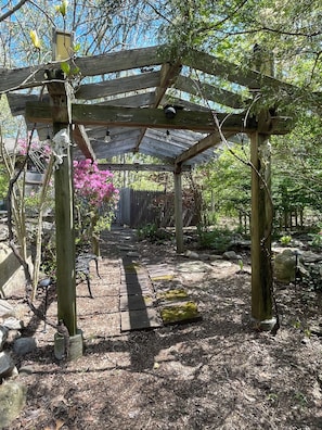 Una pérgola de madera con un sendero de ladrillo que la atraviesa.