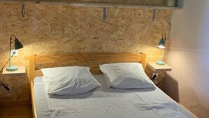 Ett sovrum med en sänggavel i trä, två sängbord med lampor och två krukväxter som hänger på väggen.