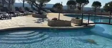 A pool area with lounge chairs and planters, surrounded by trees and a clear sky.