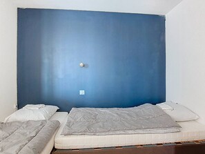 A room with a large blue headboard, a single bed with a white mattress and gray blanket, and a small bedside table. - Apartment with lake view - 6 guests (Vieux-Boucau-les-Bains)