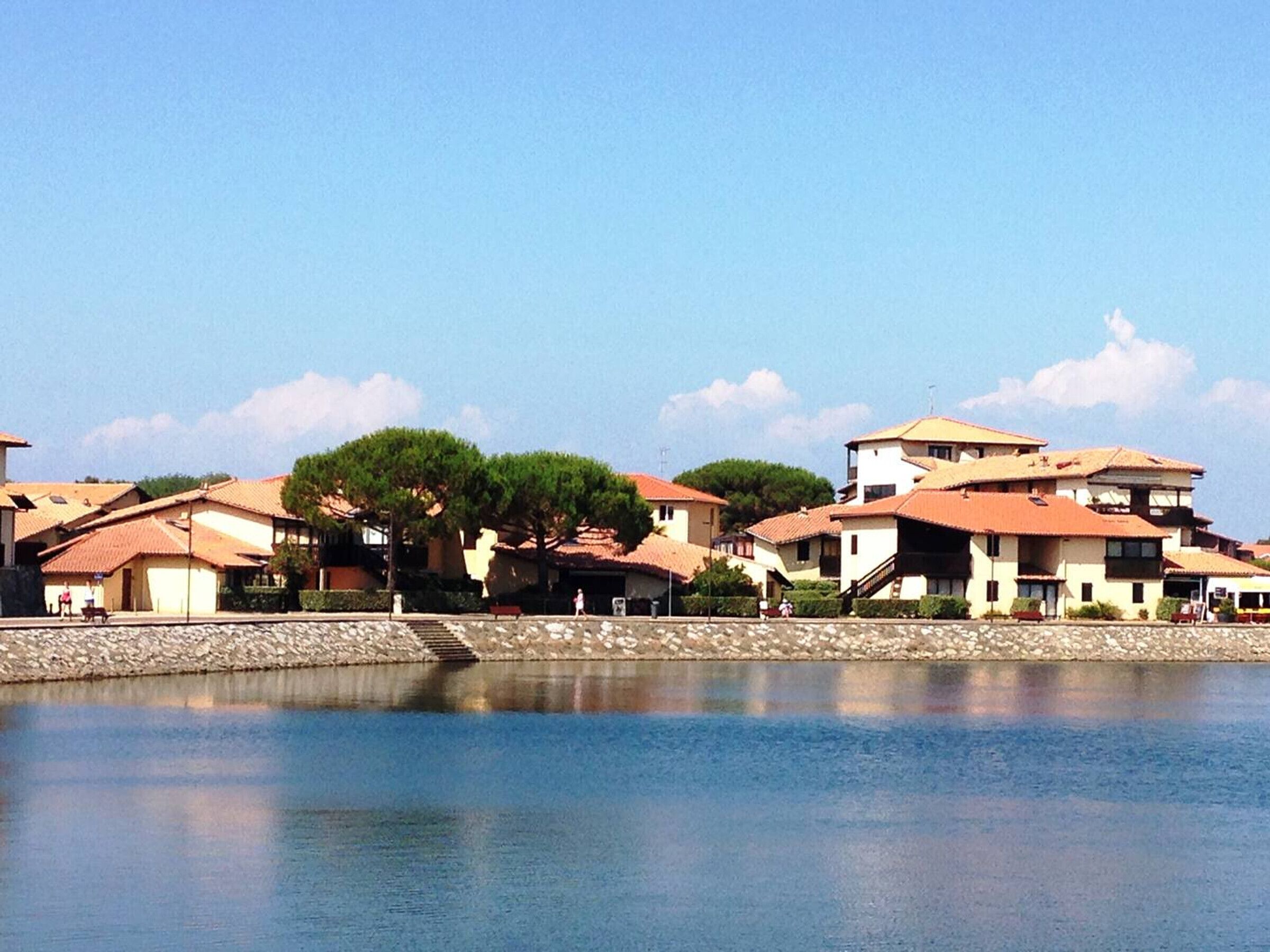 Un village côtier avec des maisons à étages, une étendue d’eau calme et un ciel dégagé.