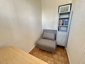 Een kleine kamer met een houten tafel, een grijze bank en een boekenkast vol boeken en een ingelijst beeld.