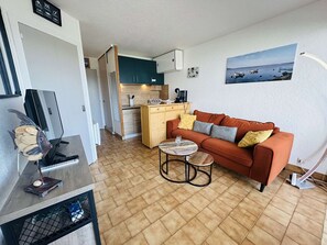 A compact living space with a kitchenette, a sofa, a coffee table, and a painting on the wall. - Bright apartment with private parking - 5 guests (Cap d'Agde)