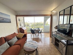 Een woonkamer met een bank, een salontafel, een televisie en een balkon met een tafel en stoelen.