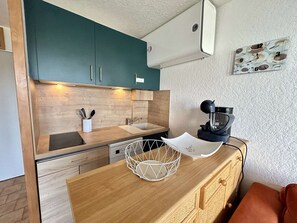 Een kleine keuken met blauwgroene kastjes, een houten aanrecht, een koffieapparaat en een mand.