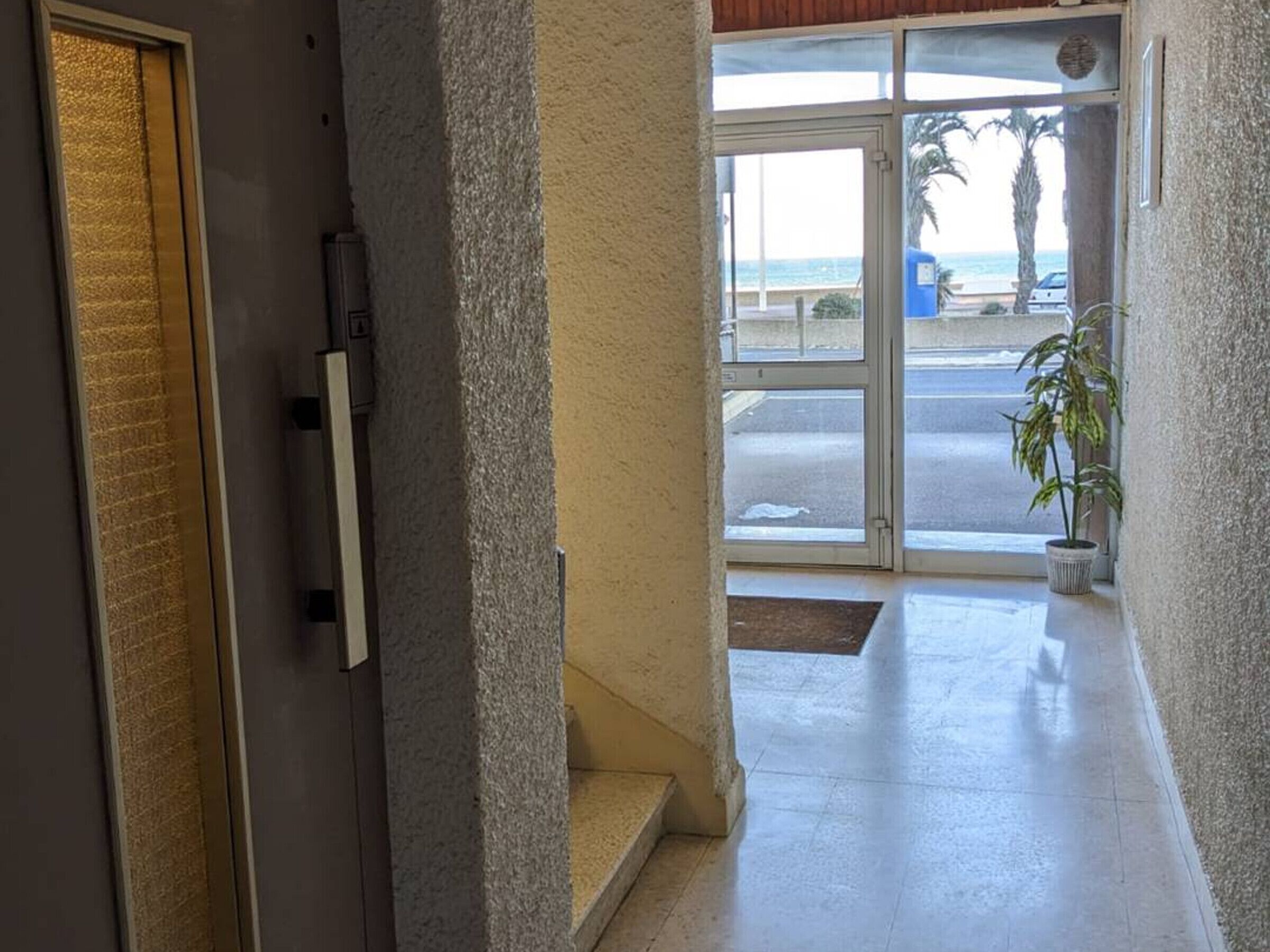 Entrada de hotel con puerta de vidrio que da a un aparcamiento y vistas a la playa.