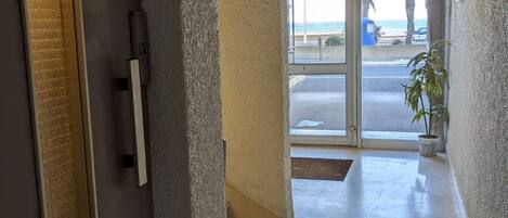 Entrada de hotel con puerta de vidrio que da a un aparcamiento y vistas a la playa.
