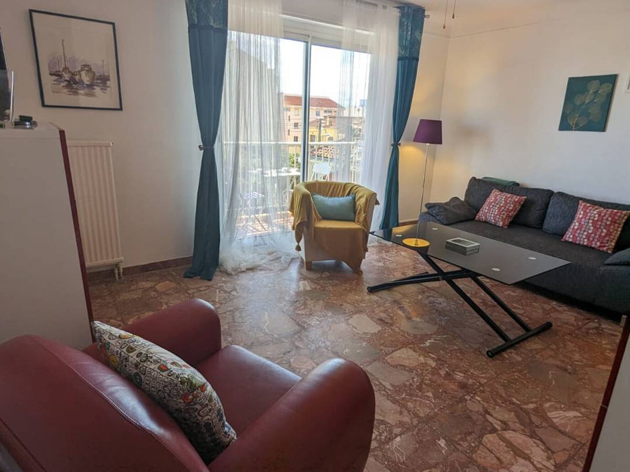 Ein Wohnzimmer mit Sofa, einem Sessel, einem Couchtisch und Blick durch ein mit Vorhängen drapiertes Fenster nach draußen.