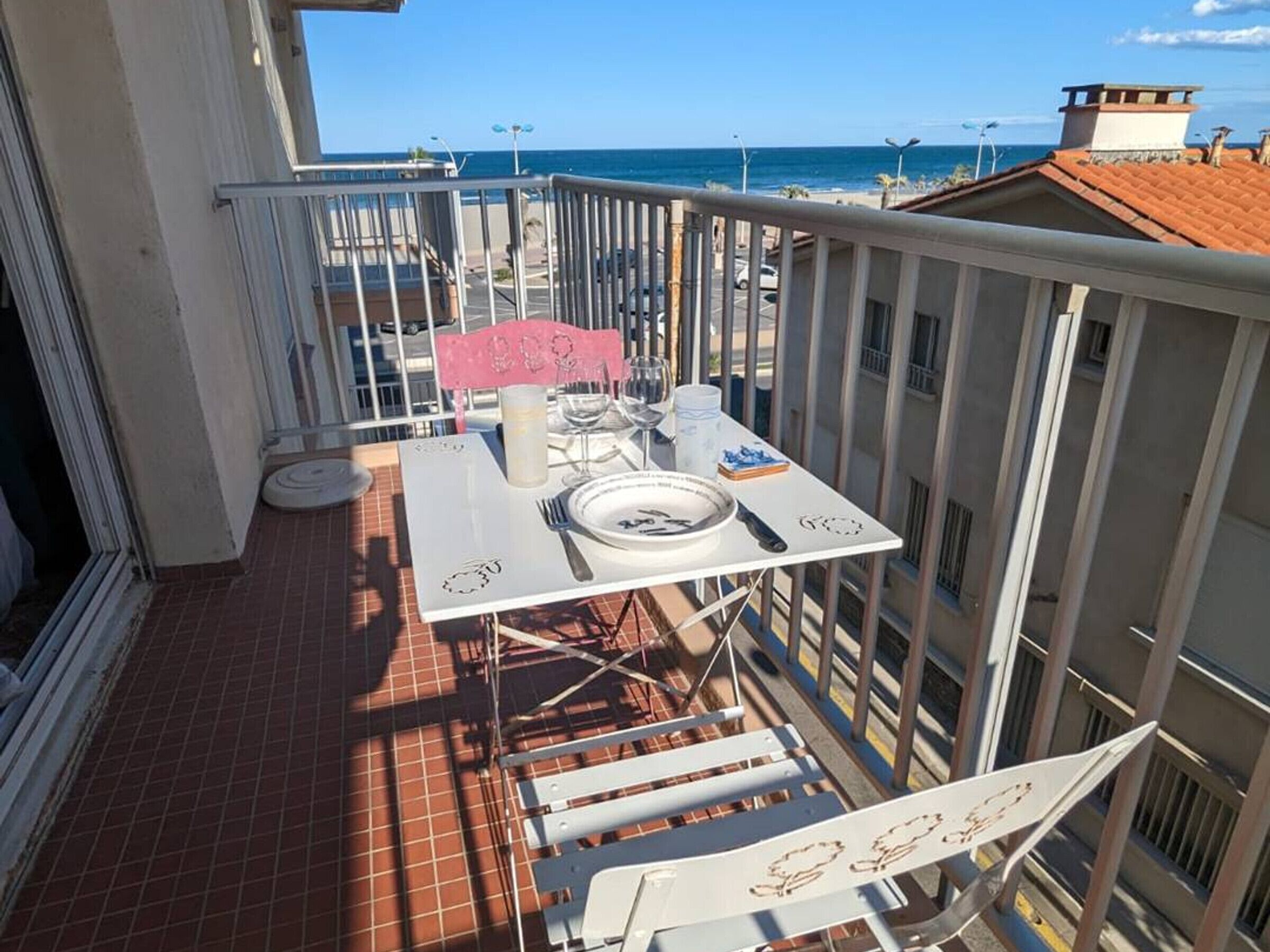 A balcony with a table set for dining, overlooking a beach and the ocean.
