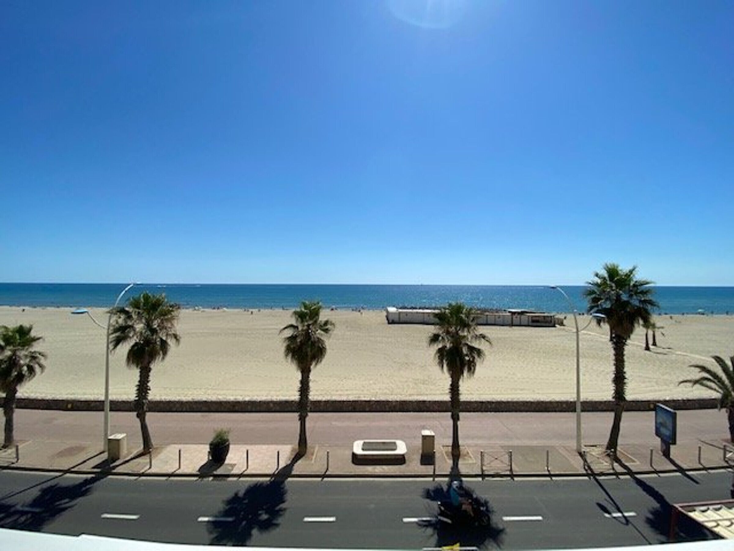 Vista da praia com palmeiras e céu claro.
